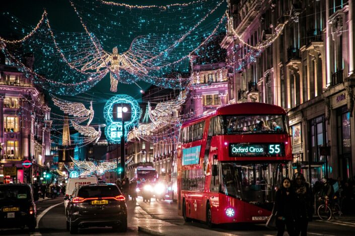 London Christmas Lights – Winter English Literature School Trips London's Regent Street illuminated with festive Christmas angel lights, featuring a red double-decker bus and historic buildings at night.