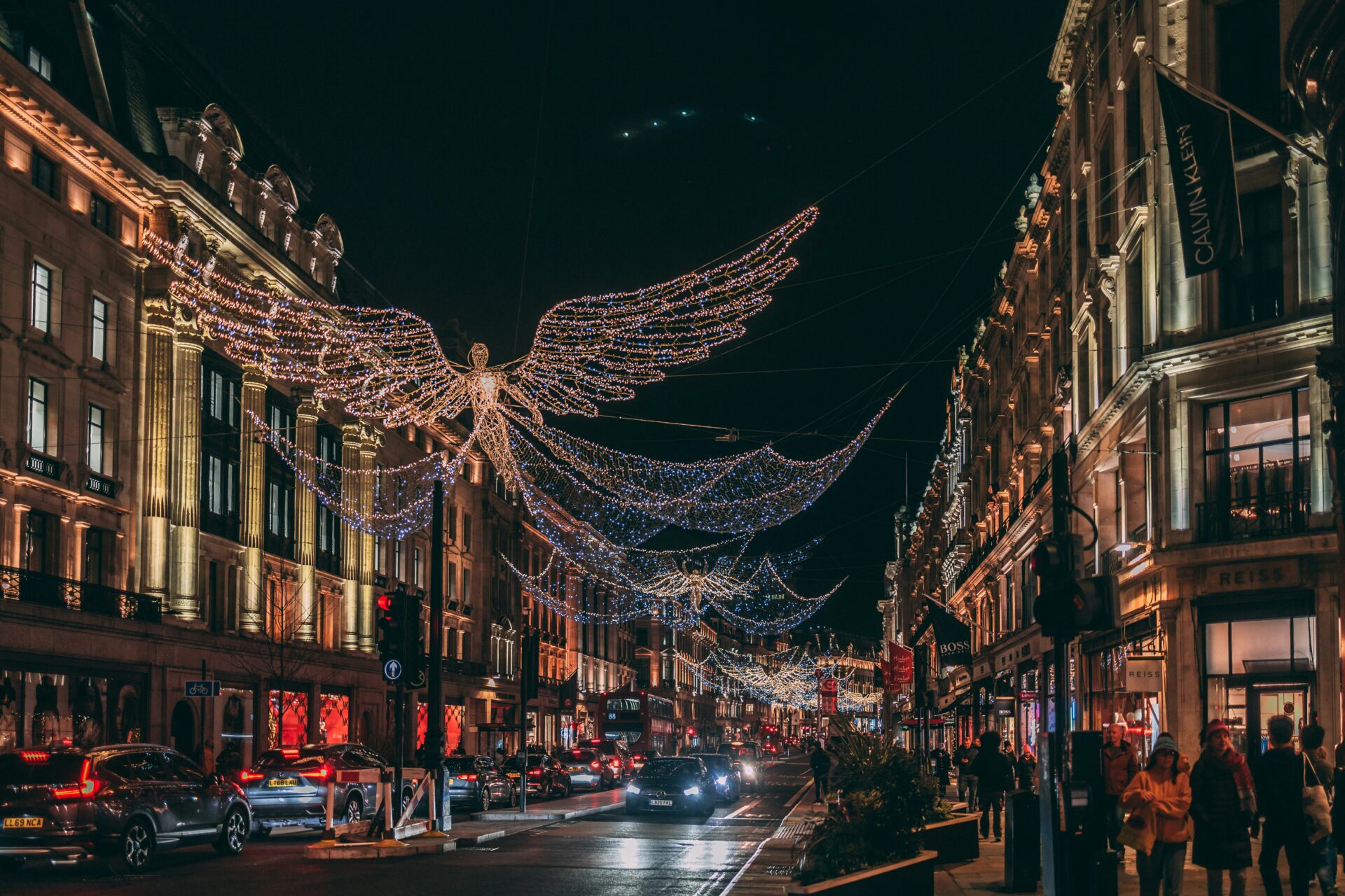Regent Street in London illuminated with Christmas angel lights, with a red double-decker bus travelling through the festive streets.
